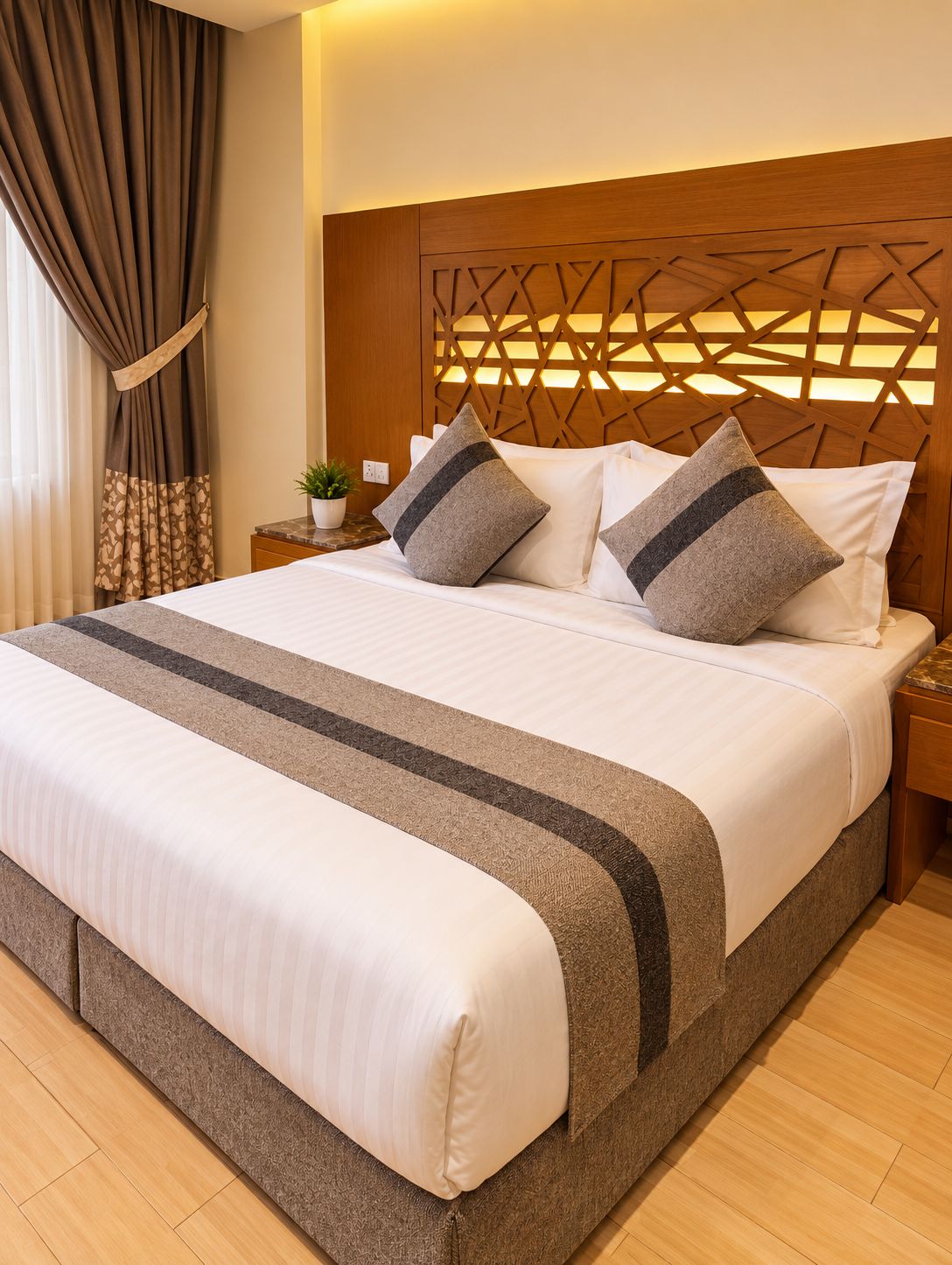 A hotel room with a large bed, a wooden headboard, and a nightstand with a plant.