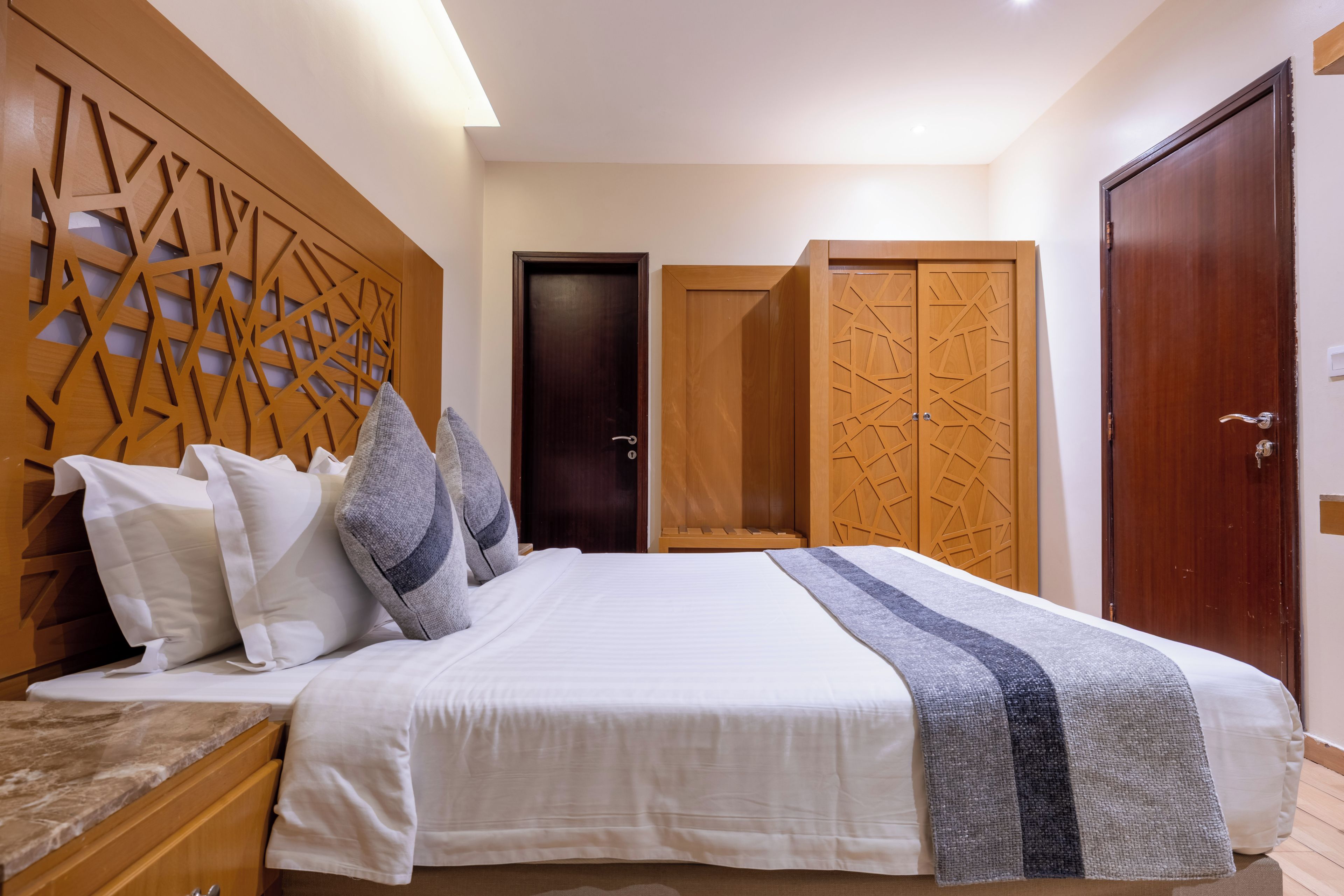 A bedroom with a bed, pillows, a wooden headboard, a wardrobe, and a door.