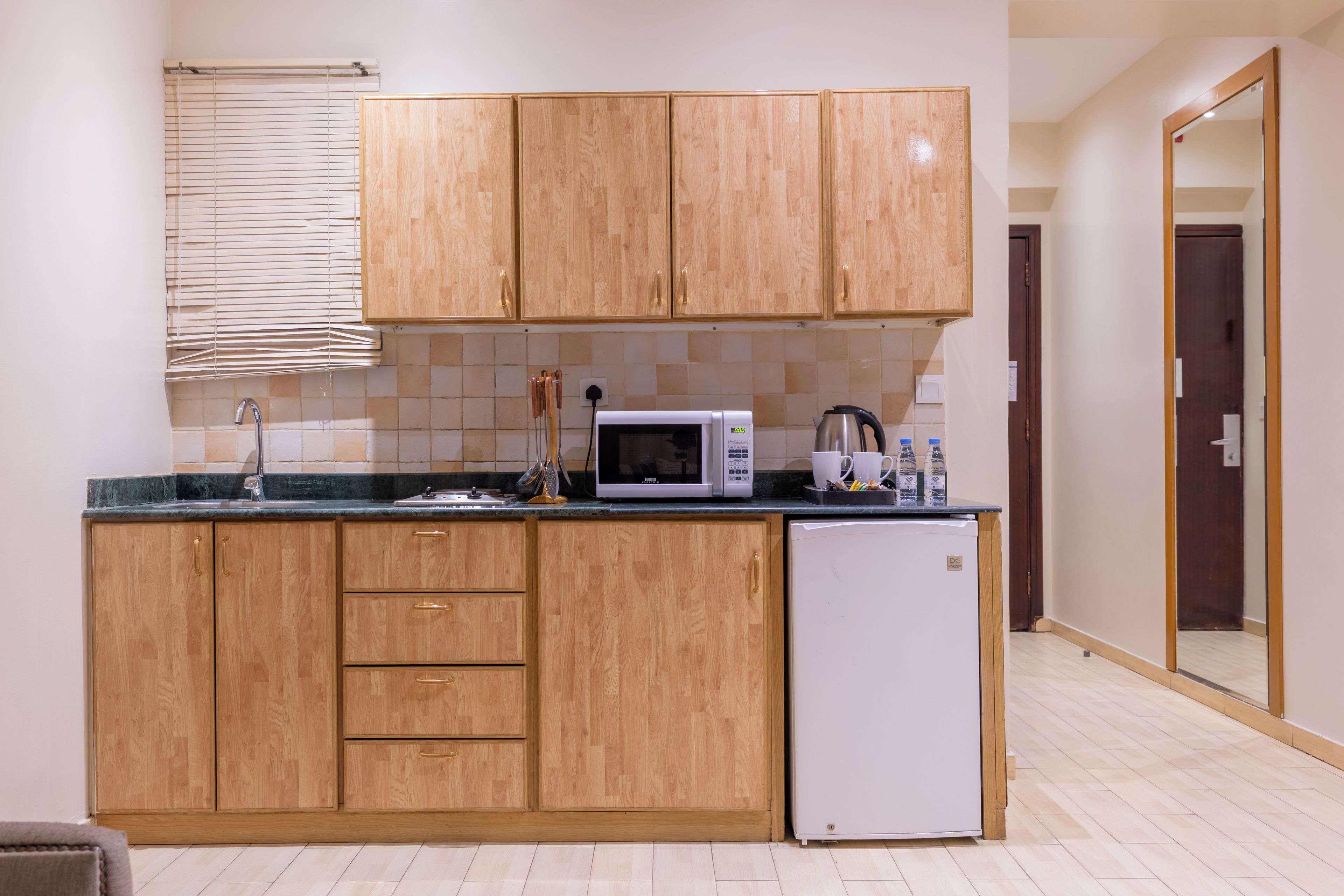 A compact kitchen with wooden cabinets, a microwave, a sink, and a small refrigerator.