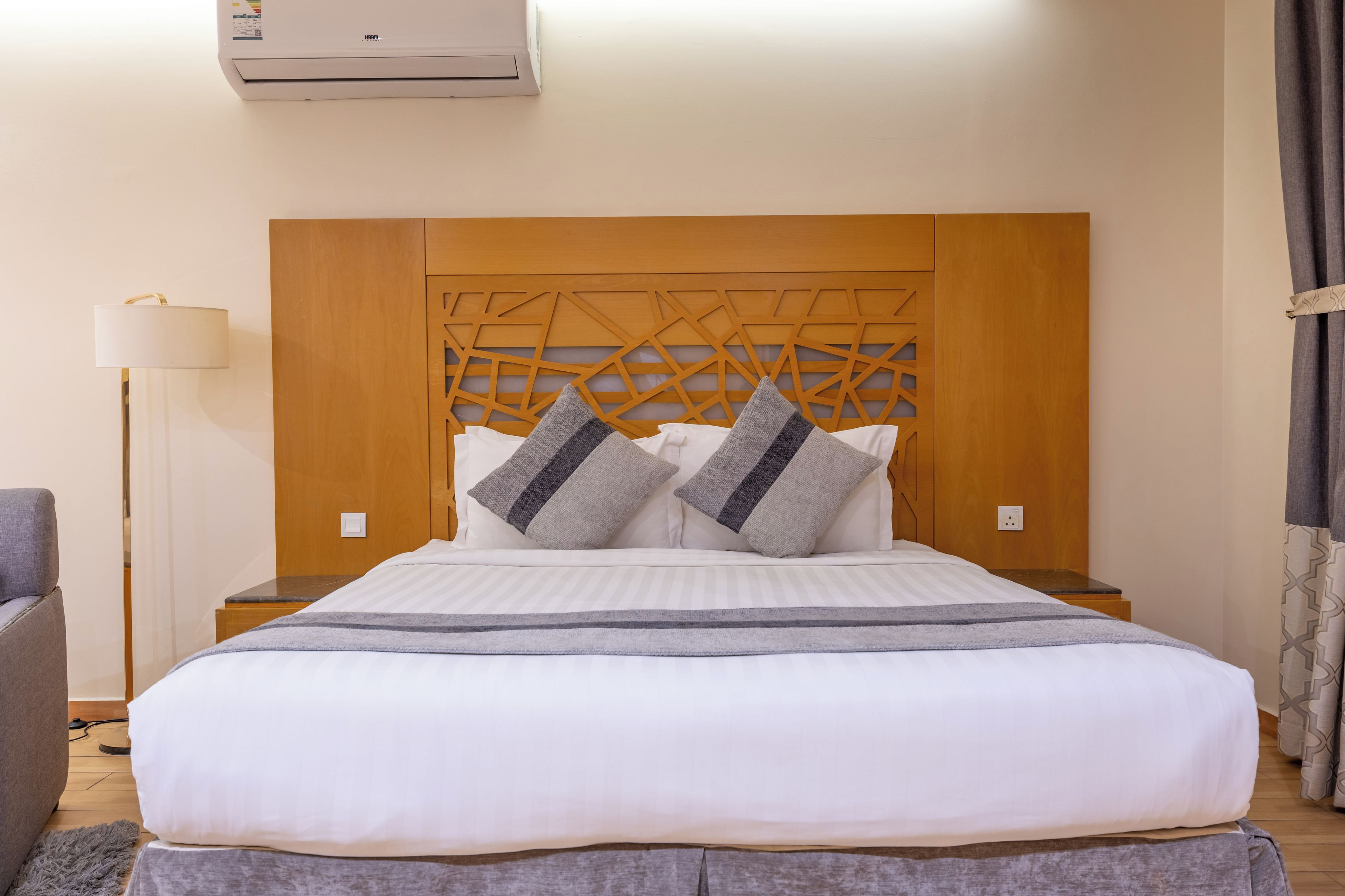 A hotel room with a large bed, a wooden headboard, two bedside tables, a lamp, and a curtain.