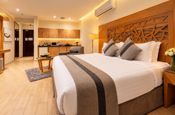 A modern hotel room with a large bed, a wooden headboard, a small kitchenette, and a separate seating area. - Al Muhaidb Residence Al Malaz 4 - Economic (Riyadh)