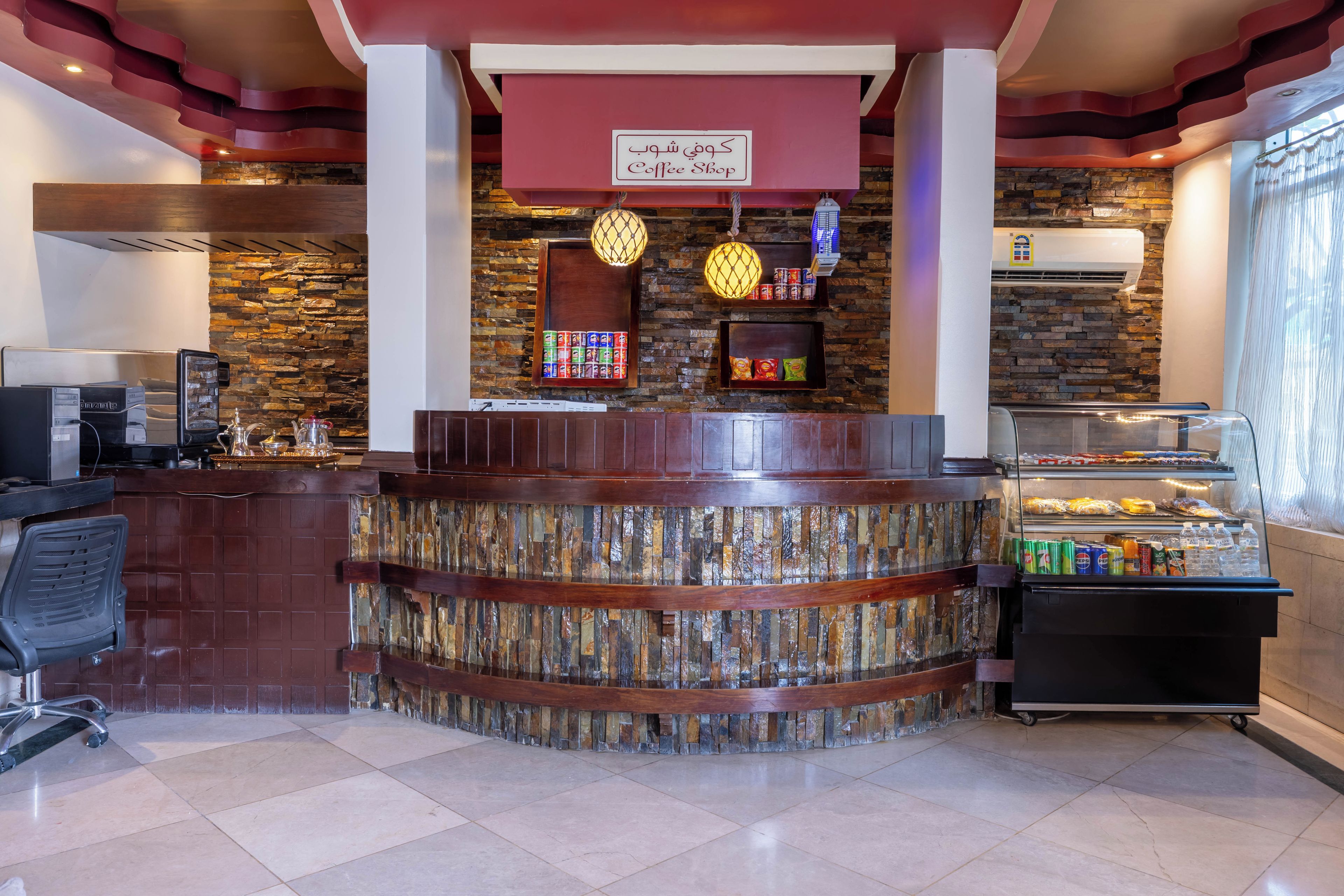 A coffee shop interior with a stone wall, a counter with a sign, and a display case with snacks.