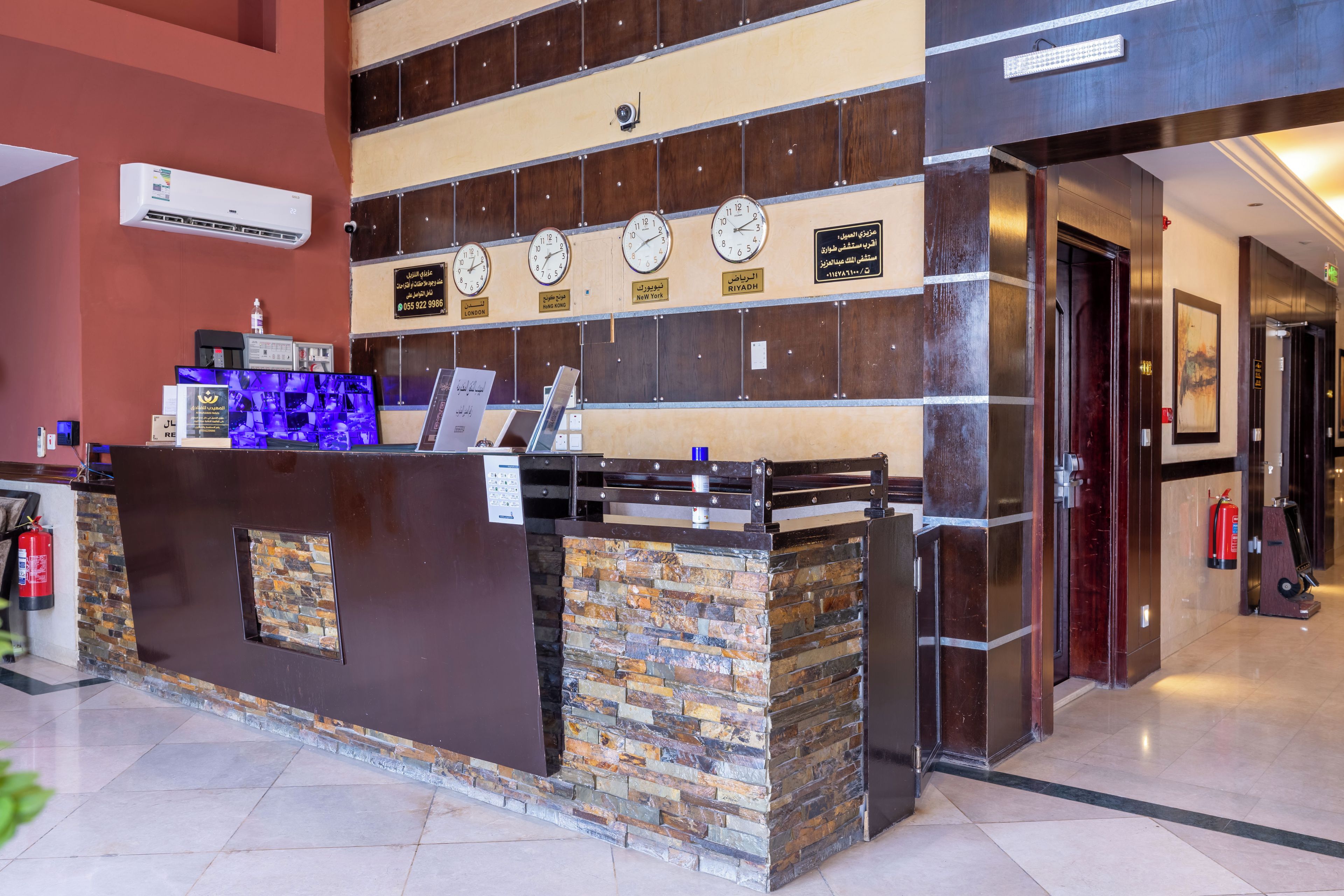 A hotel reception desk with clocks displaying different time zones, a fire extinguisher, and a fire alarm.