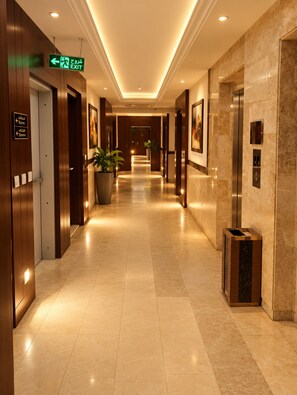 A hotel corridor with an exit sign, elevator, and a trash bin. - Al Muhaidb Residence Al Malaz 4 - Economic (Riyadh)
