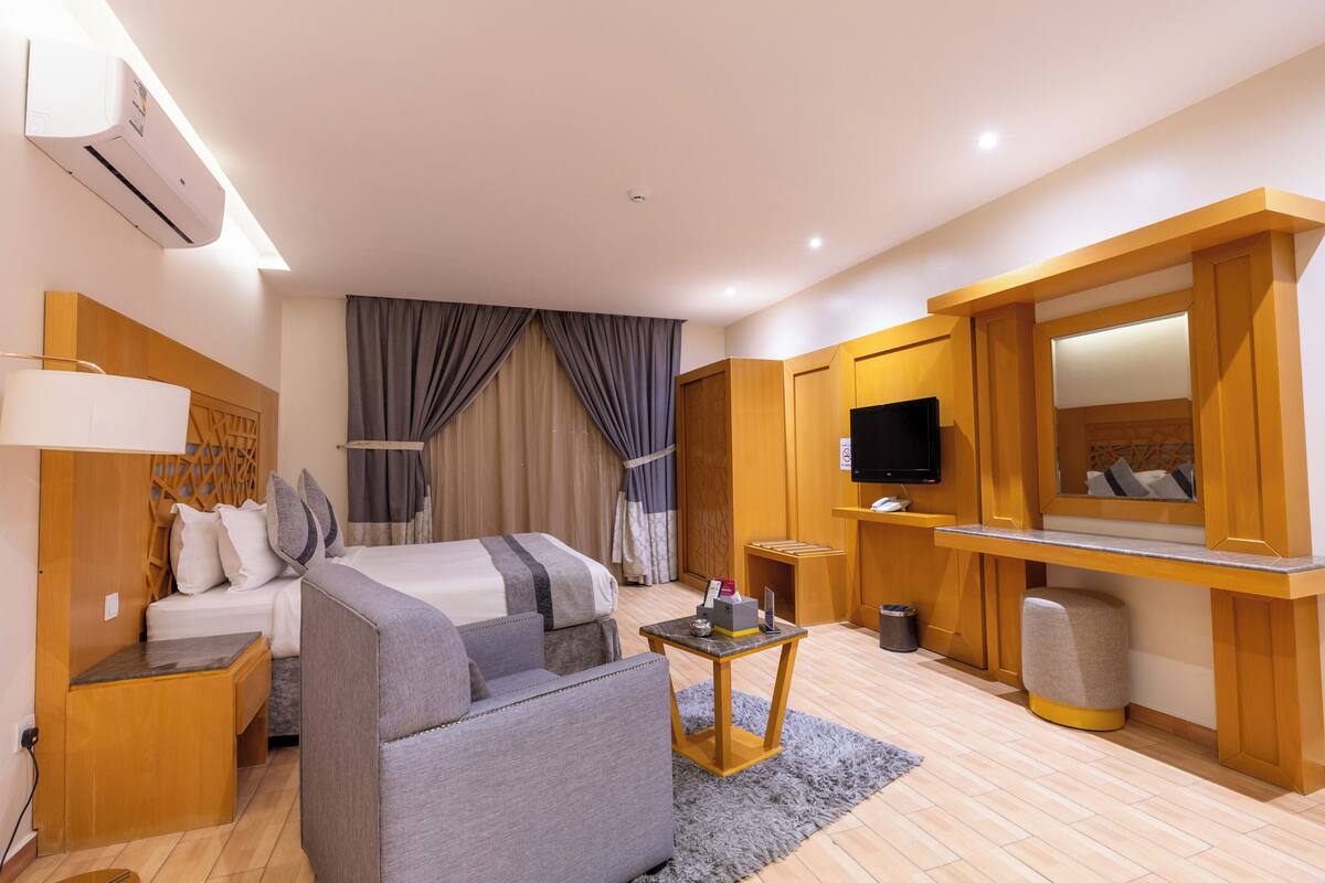 A hotel room with a bed, a sofa, a TV, a small table, and a mirror.
