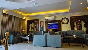 A modern living room with a sectional sofa, a flat-screen TV, and a decorative wall clock. - DAR NEYAARA SERVICED APARTMENTS - Economic (Riyadh)