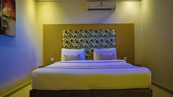 Habitación de hotel con una cama grande, cabecera con papel tapiz floral y un equipo de aire acondicionado en la pared.