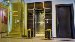 A modern elevator with glass doors, a fire extinguisher, and a dark door. - DAR NEYAARA SERVICED APARTMENTS - Economic (Riyadh)