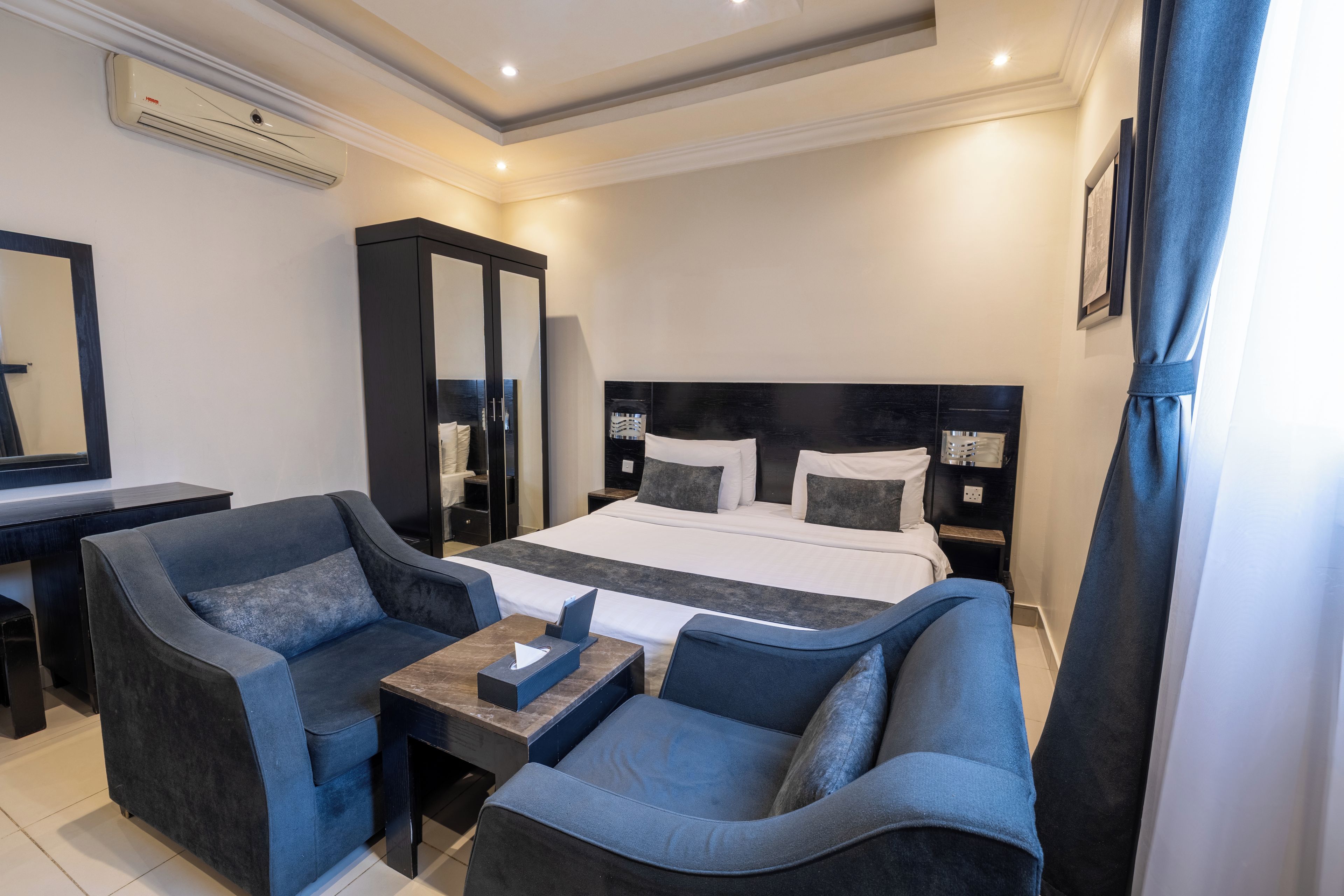 Una camera d'albergo con un letto, due poltrone, un tavolino, un guardaroba e uno specchio.