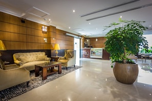 A lobby with a sofa, armchairs, a coffee table, a large potted plant, and a reception desk. - Al Muhaidb Residence PALASTINE - Economic (Jeddah)