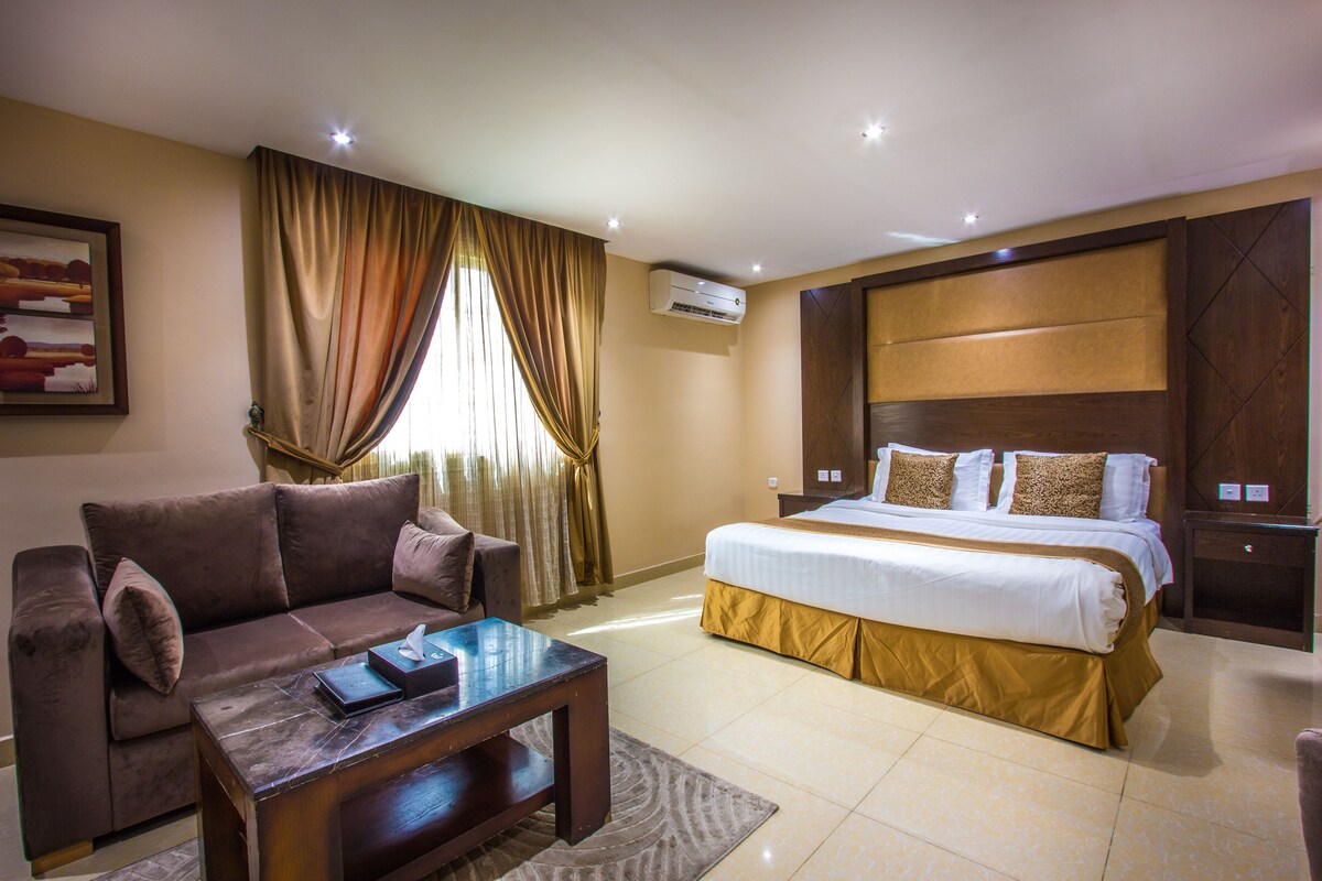 A hotel room with a bed, a sofa, a coffee table, and a painting on the wall.