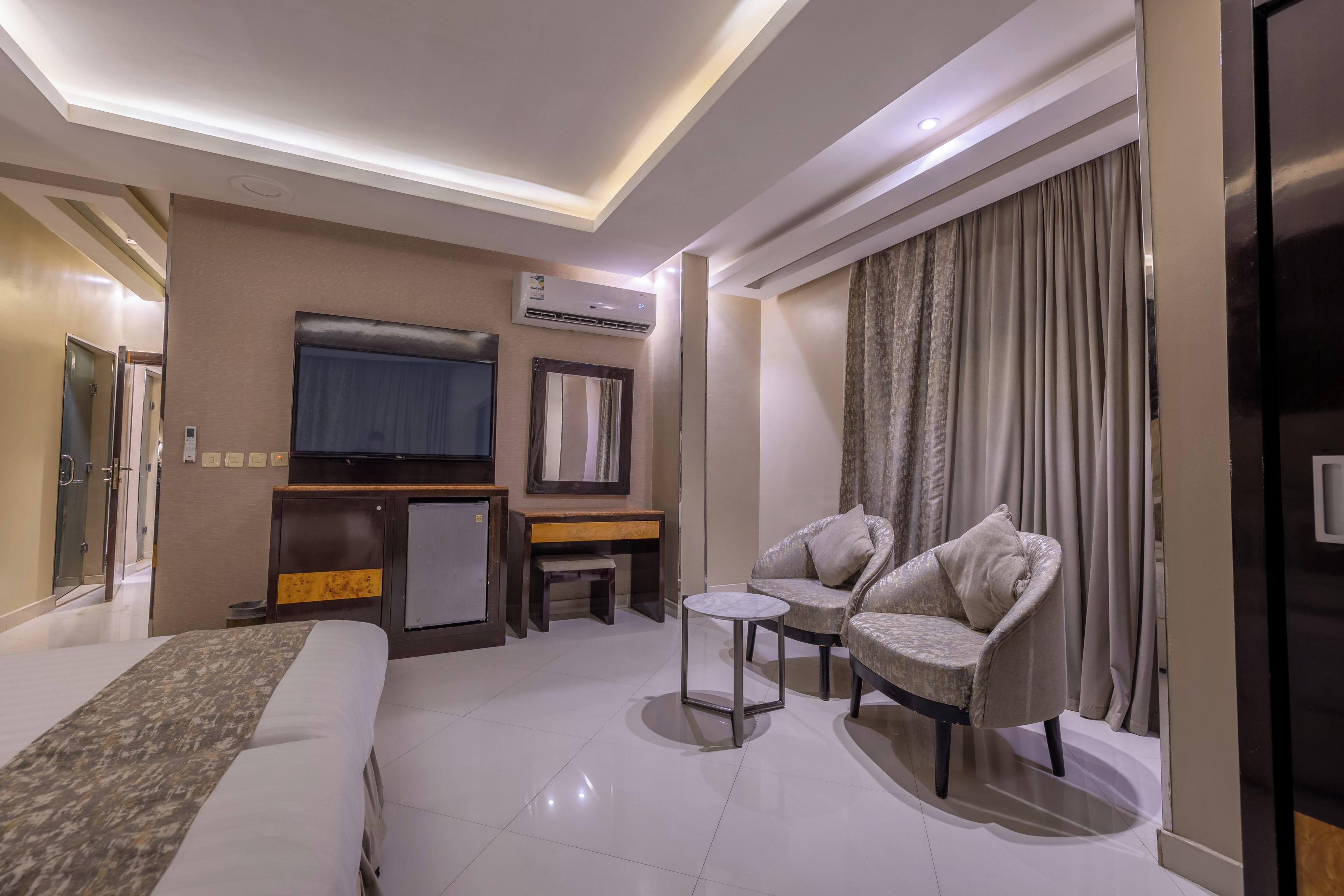 A hotel room with a bed, a desk, a TV, and two armchairs.