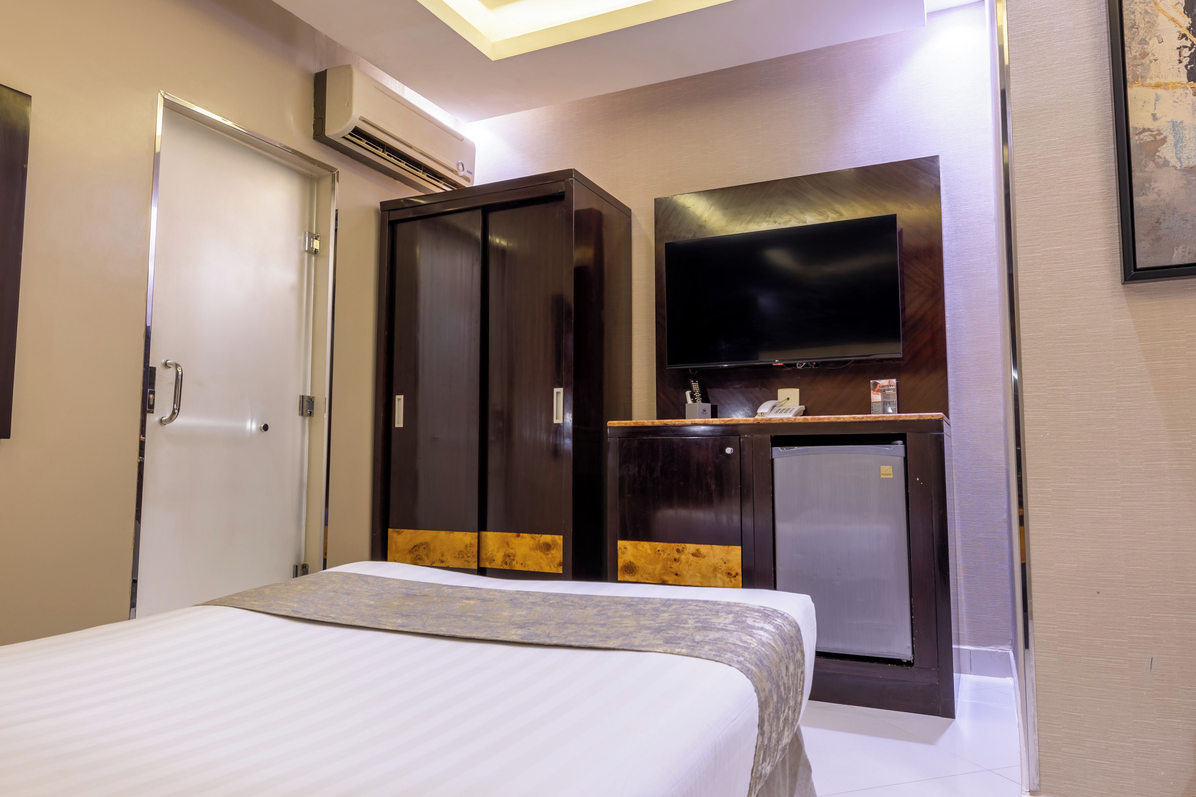 Una habitación de hotel con cama, armario, televisión y un refrigerador pequeño.