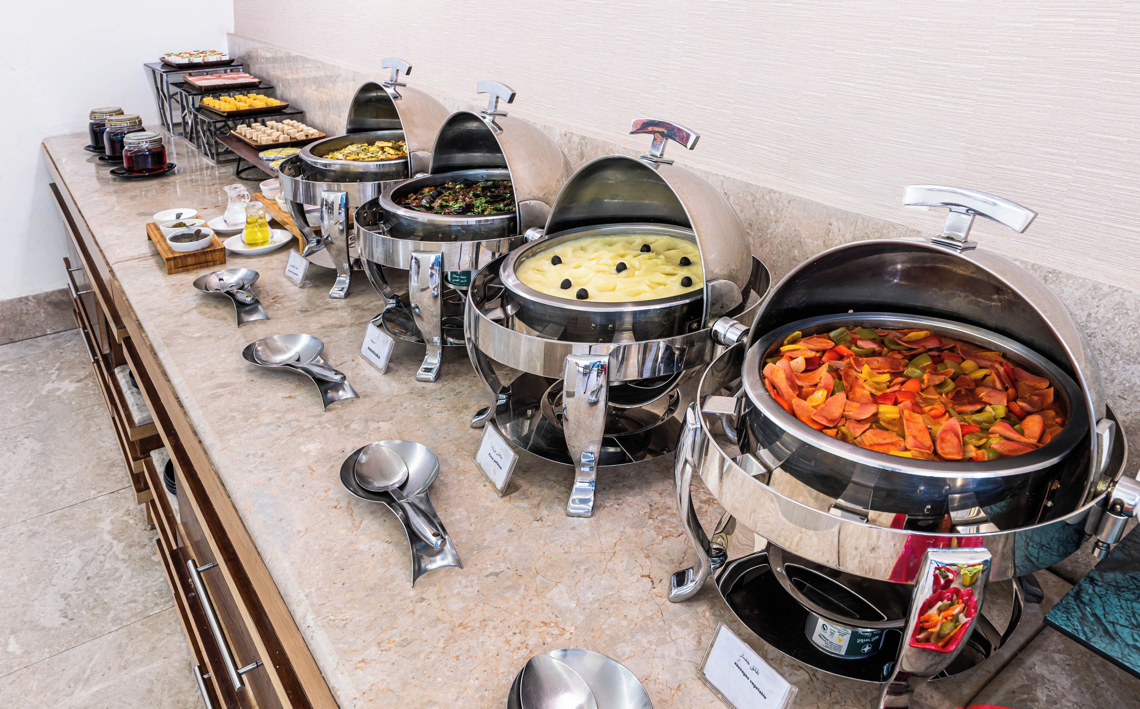 Montaje tipo buffet con varias estaciones de comida, incluyendo una olla grande de guiso y varios platos más pequeños con diferentes alimentos.