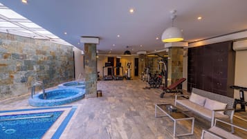 A modern indoor pool area with a stone wall, a seating area with a sofa, and exercise equipment.