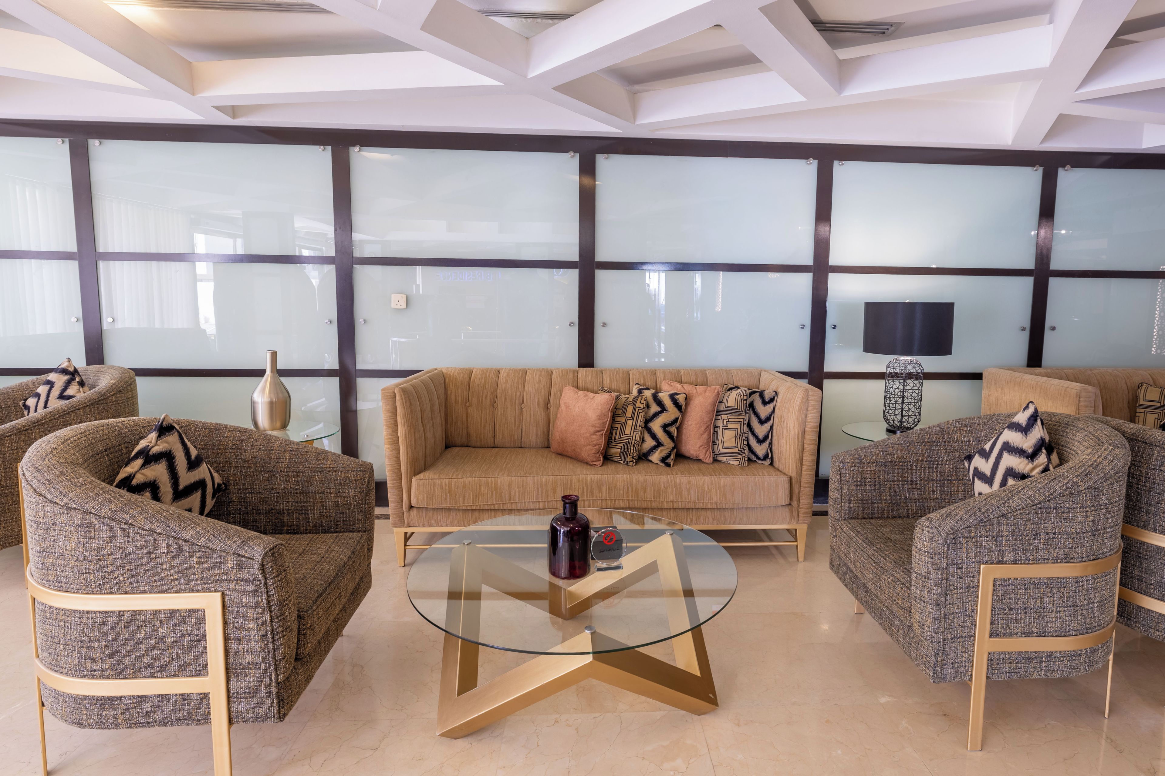 Un área de estar moderna con un sofá, sillones y una mesa de centro de vidrio.