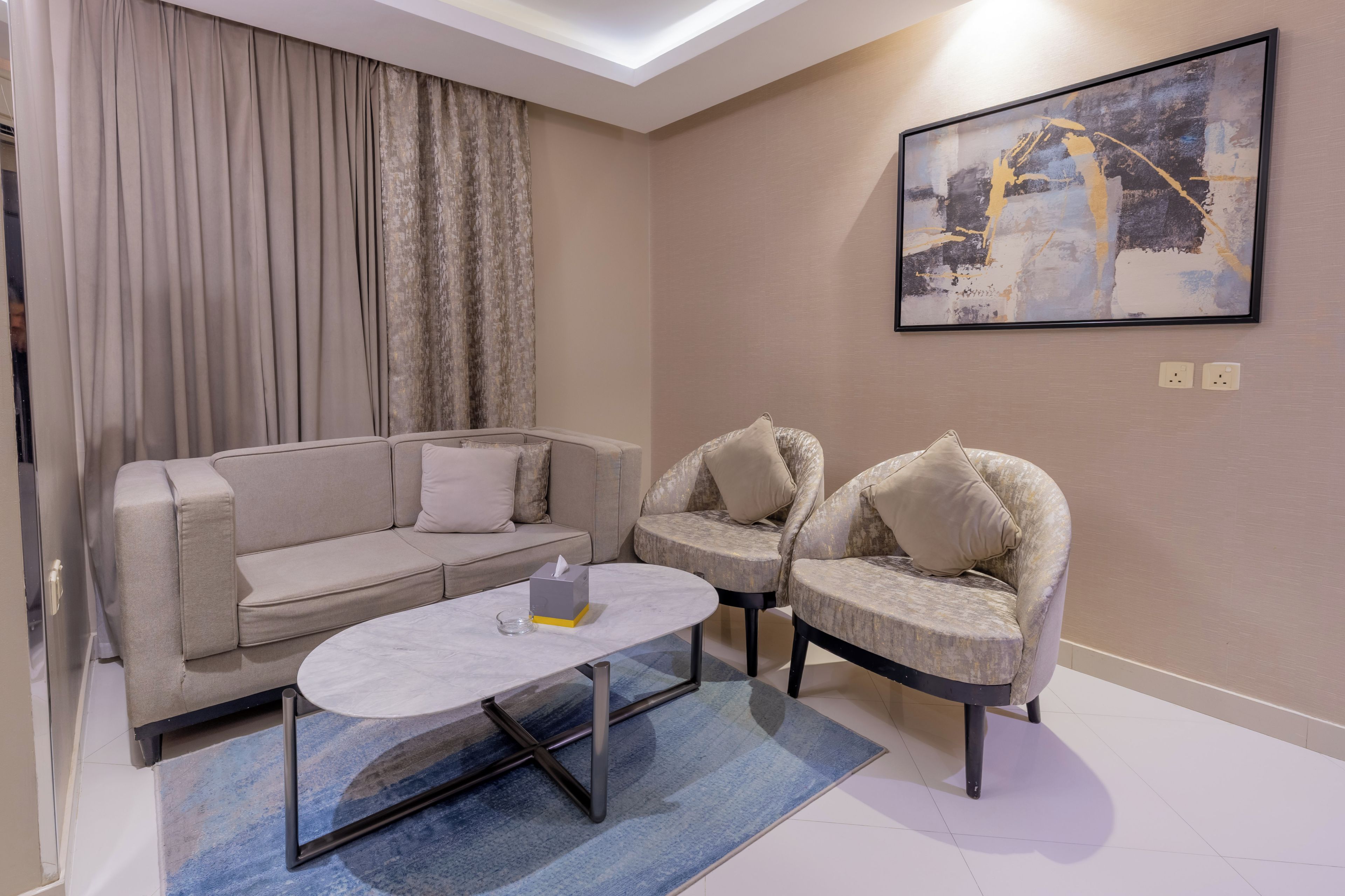 A modern living room with a sofa, two armchairs, a coffee table, and a painting on the wall.