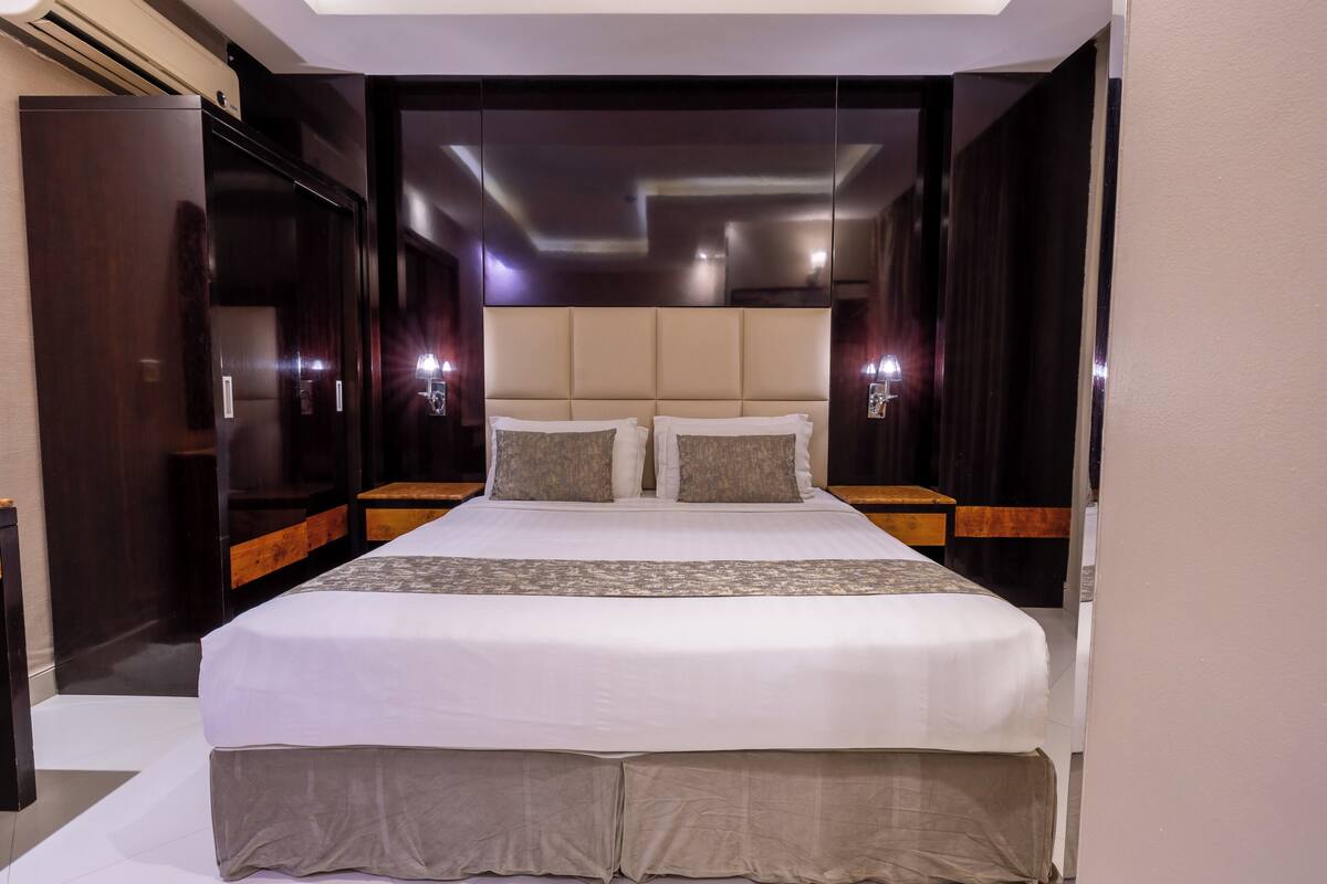 Une chambre d’hôtel moderne avec un grand lit, une tête de lit en bois et des tables de chevet.