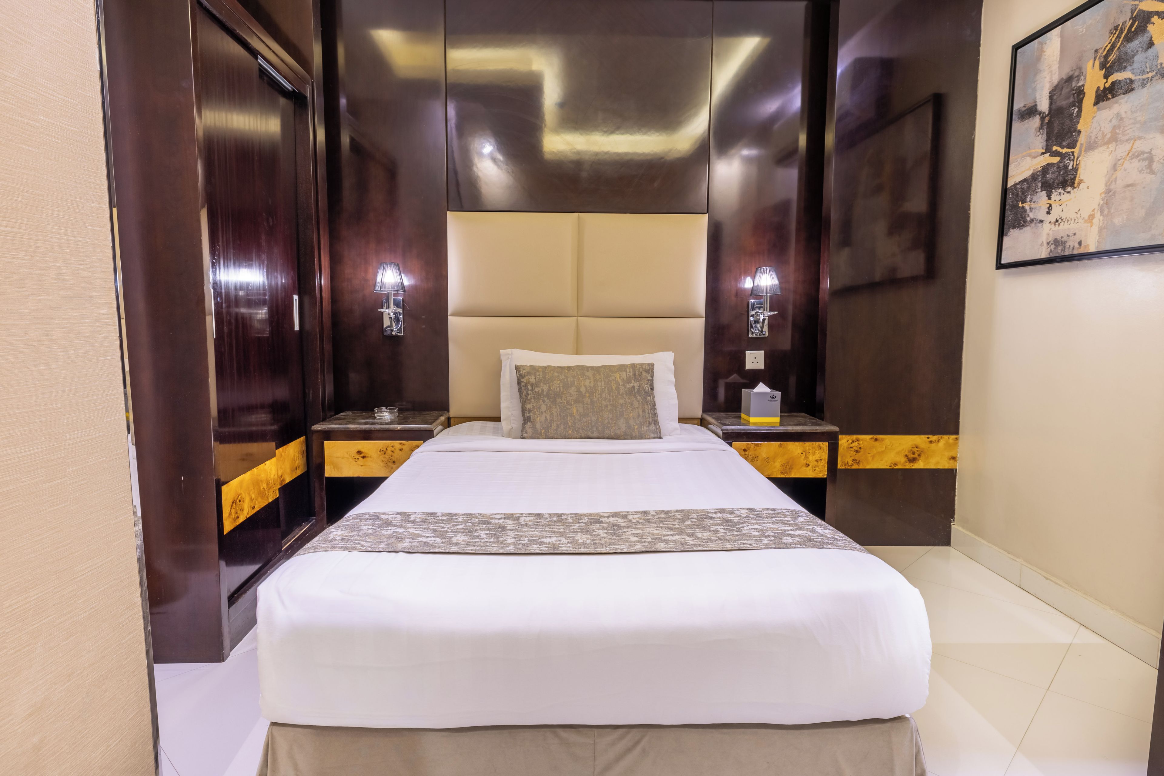 A hotel room with a large bed, two bedside tables with lamps, a headboard, and a painting on the wall.