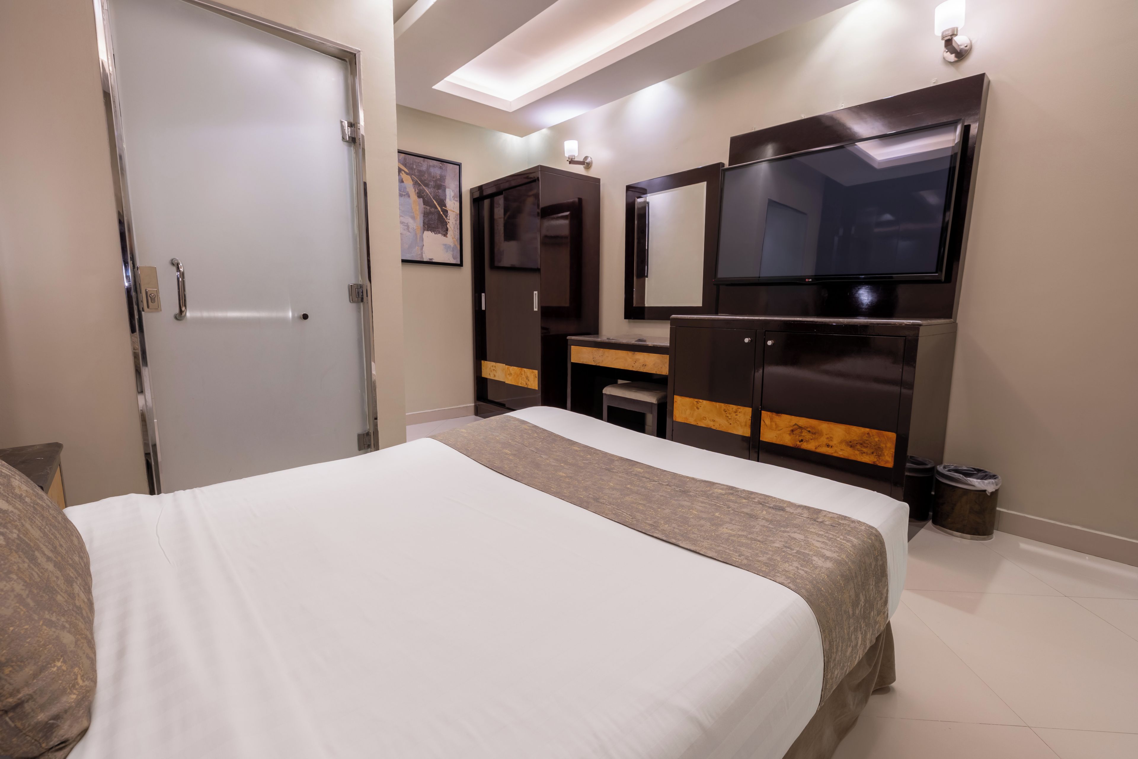 A hotel room with a bed, a desk, a mirror, and a television.