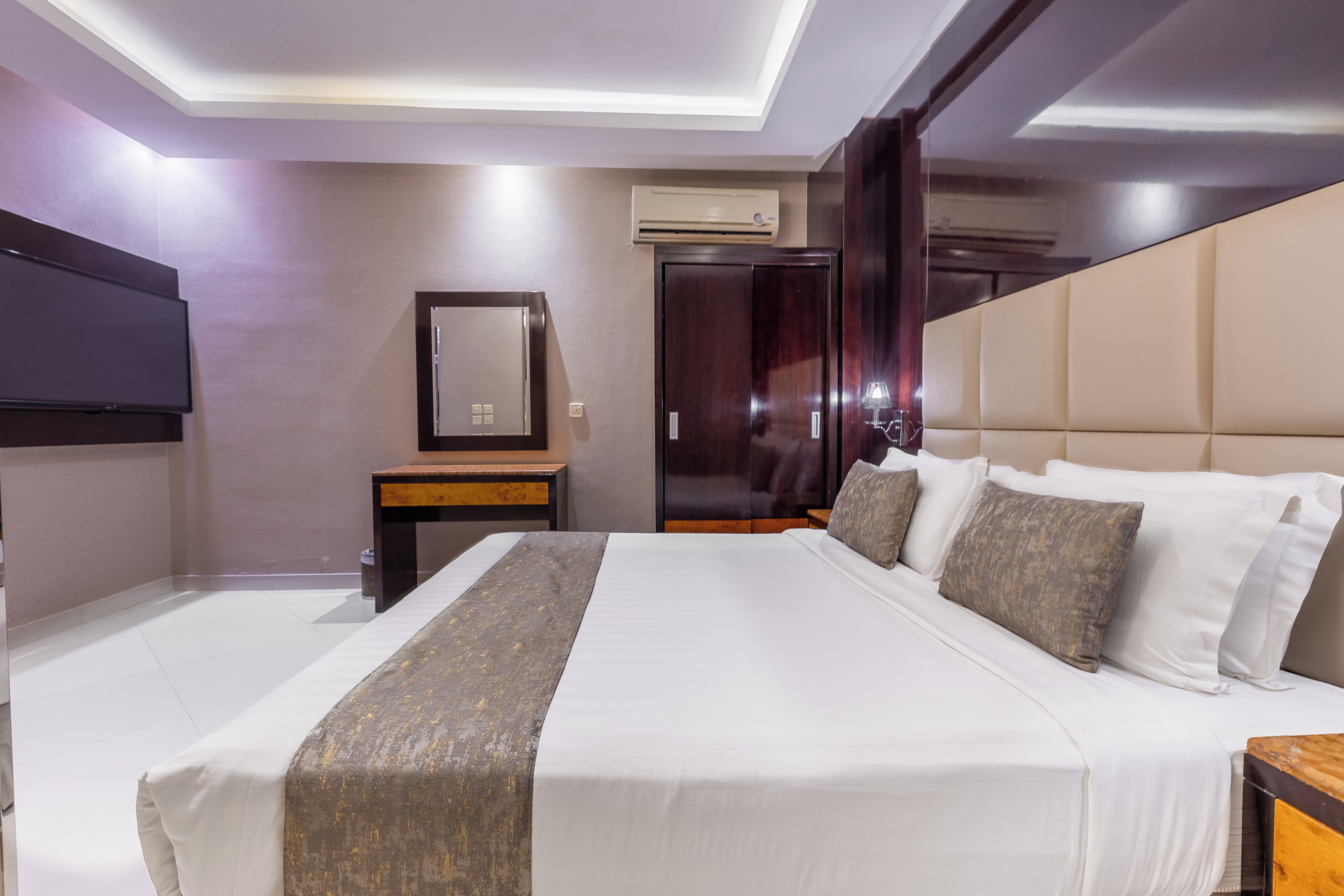 A hotel room with a large bed, a flat-screen TV mounted on the wall, a small table, and a wardrobe.