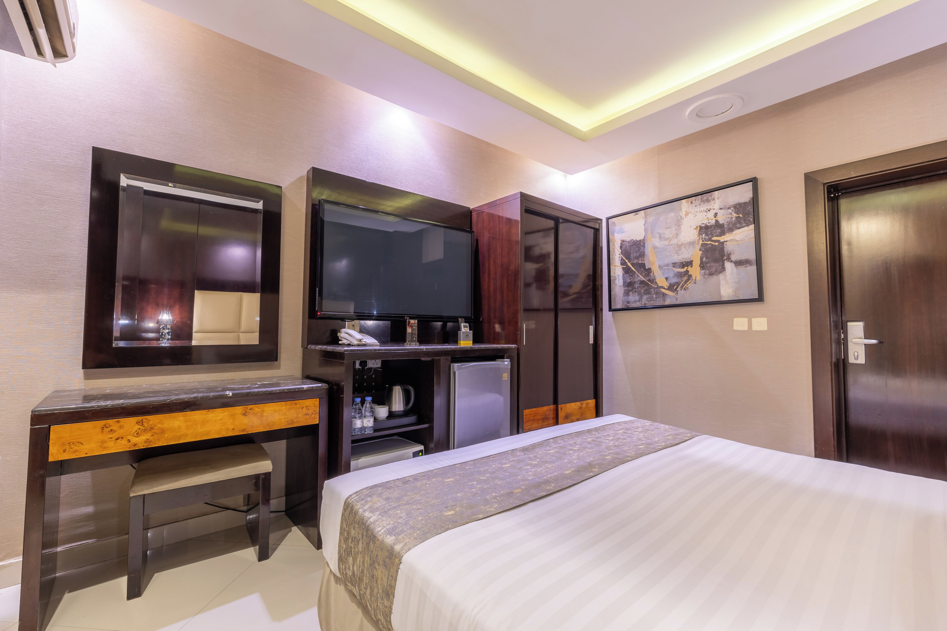 A hotel room with a bed, a desk, a television, a wardrobe, and a painting on the wall.