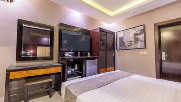 A hotel room with a bed, a desk, a television, a wardrobe, and a painting on the wall.