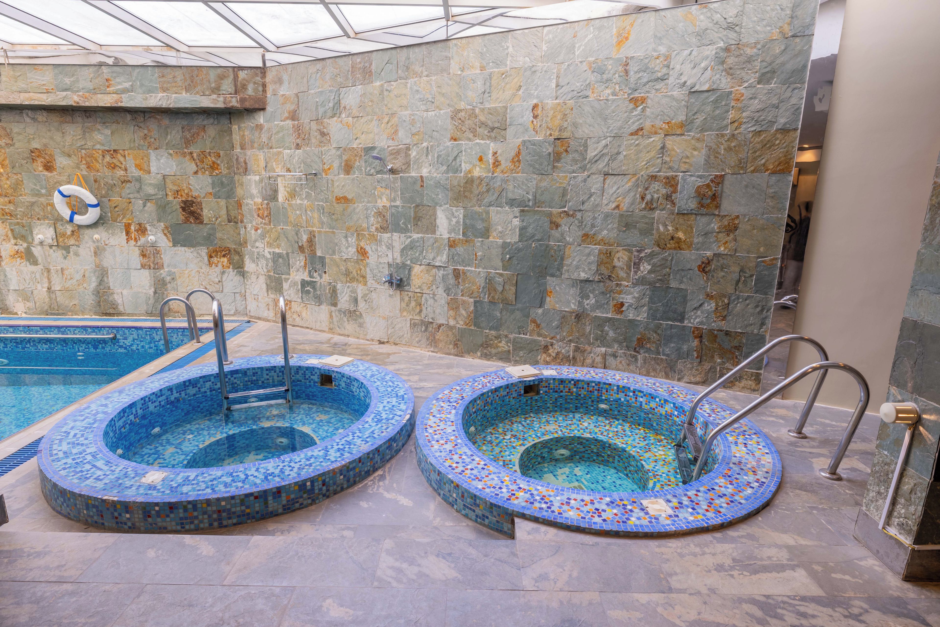 Un espace piscine intérieure doté de deux bains à remous et d’un plafond en verre.