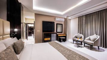 A modern hotel room with a large bed, a flat-screen TV, a desk with two chairs, and a large window with curtains.