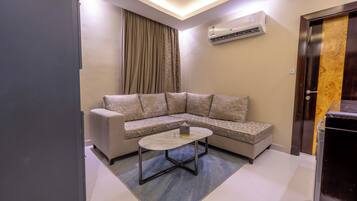 A modern living room with a sectional sofa, a small round coffee table, and an air conditioning unit mounted on the wall.