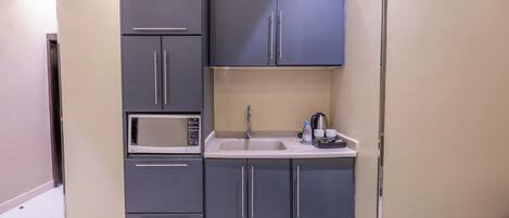 Una cocina compacta con microondas, lavamanos y armarios.