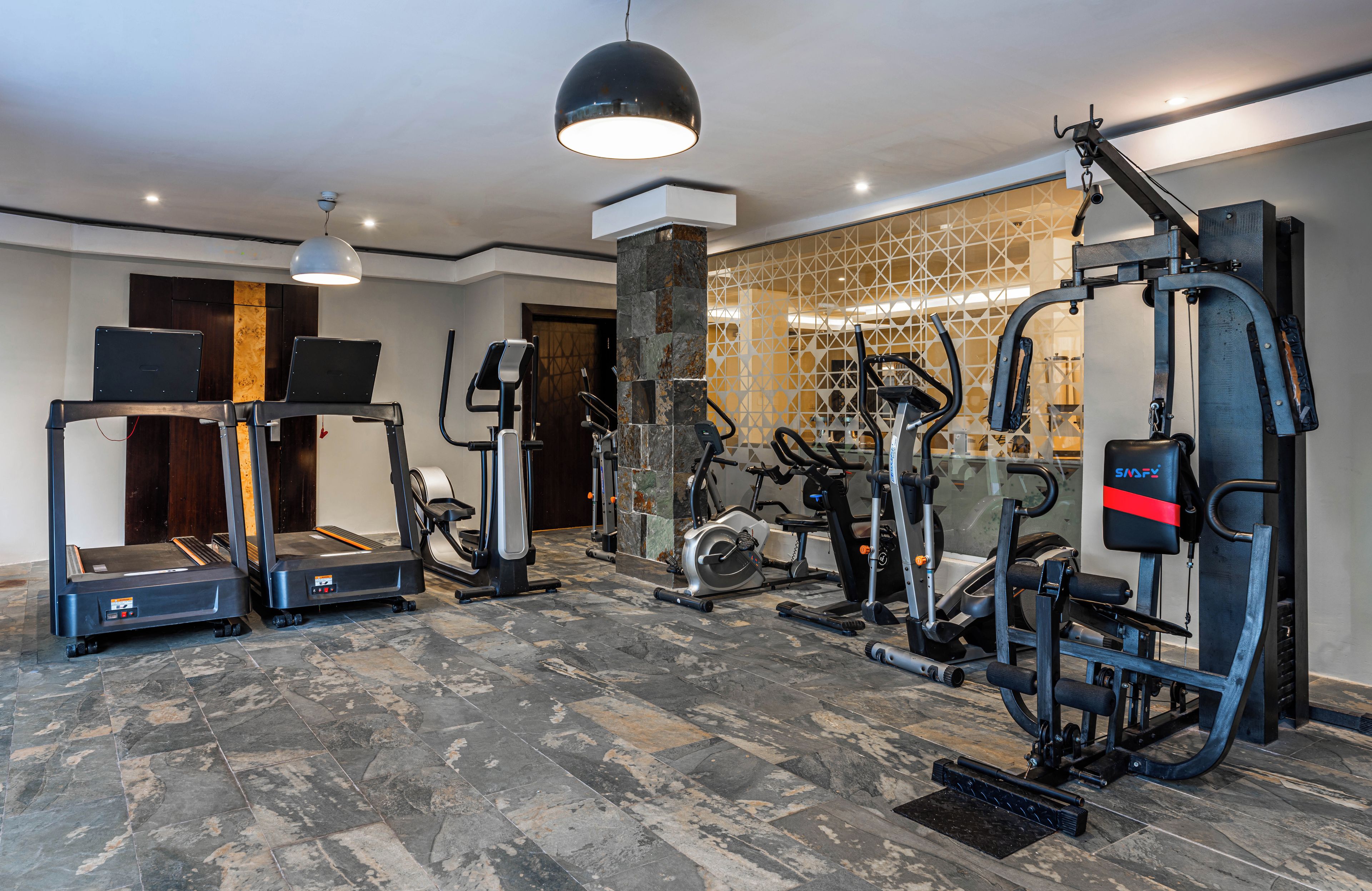 Un gimnasio con máquinas de cardio, equipo de entrenamiento con pesas y un espejo grande.