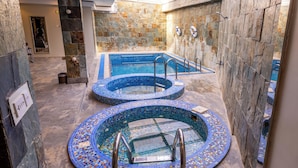 A spa area with two circular hot tubs and a rectangular pool, surrounded by stone walls and tiled flooring.