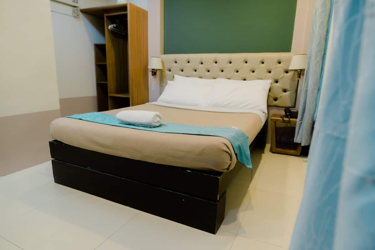Cama bem arrumada com cabeceira bege, peseira preta e manta azul.