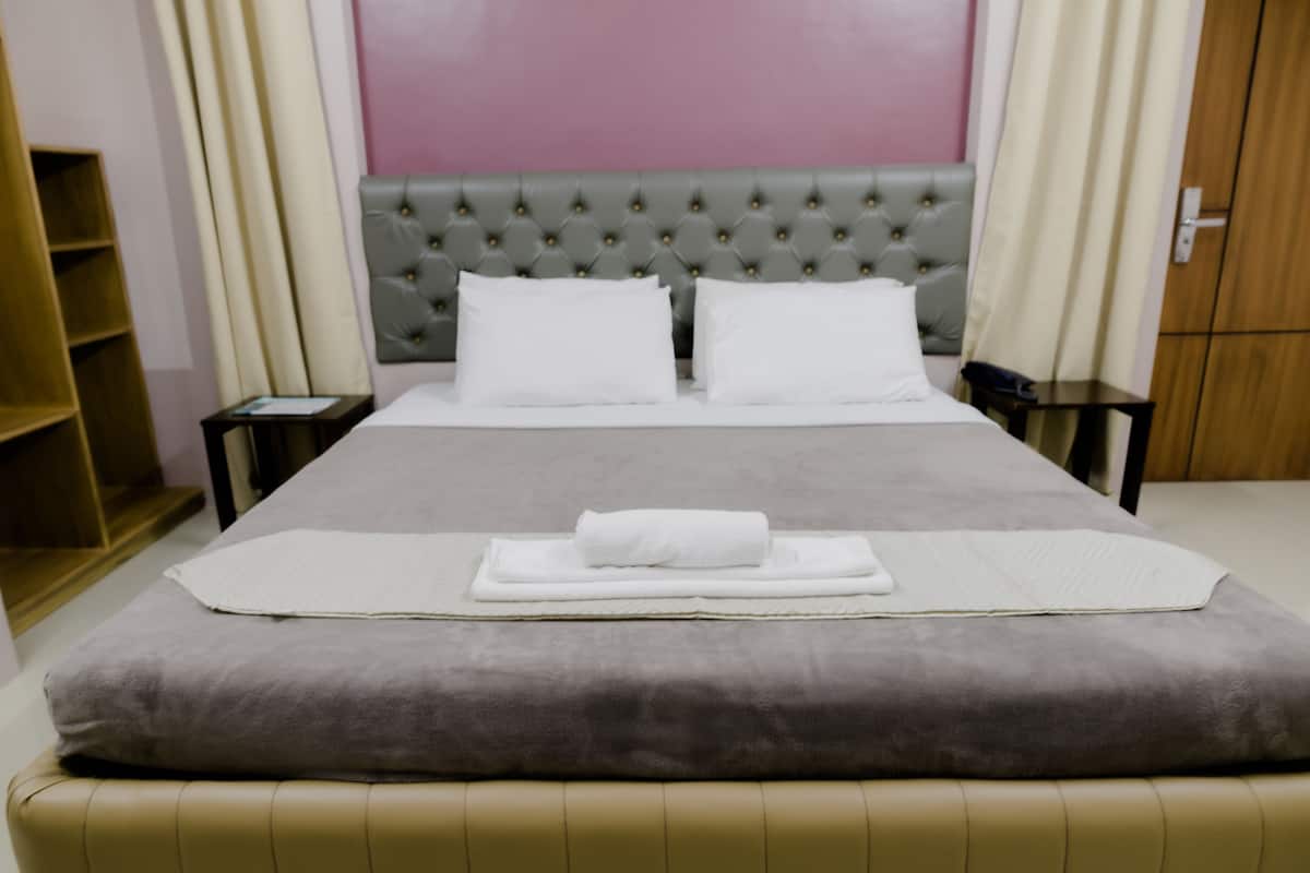 Cama bem arrumada com edredom cinza e branco, cabeceira estofada cinza e travesseiros brancos.