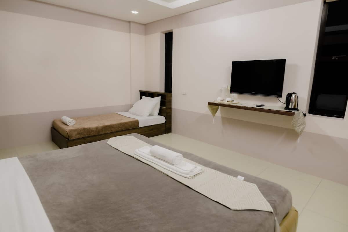 Quarto de hotel moderno com uma cama grande, uma cama menor, uma televisão e uma prateleira com artigos de higiene pessoal.