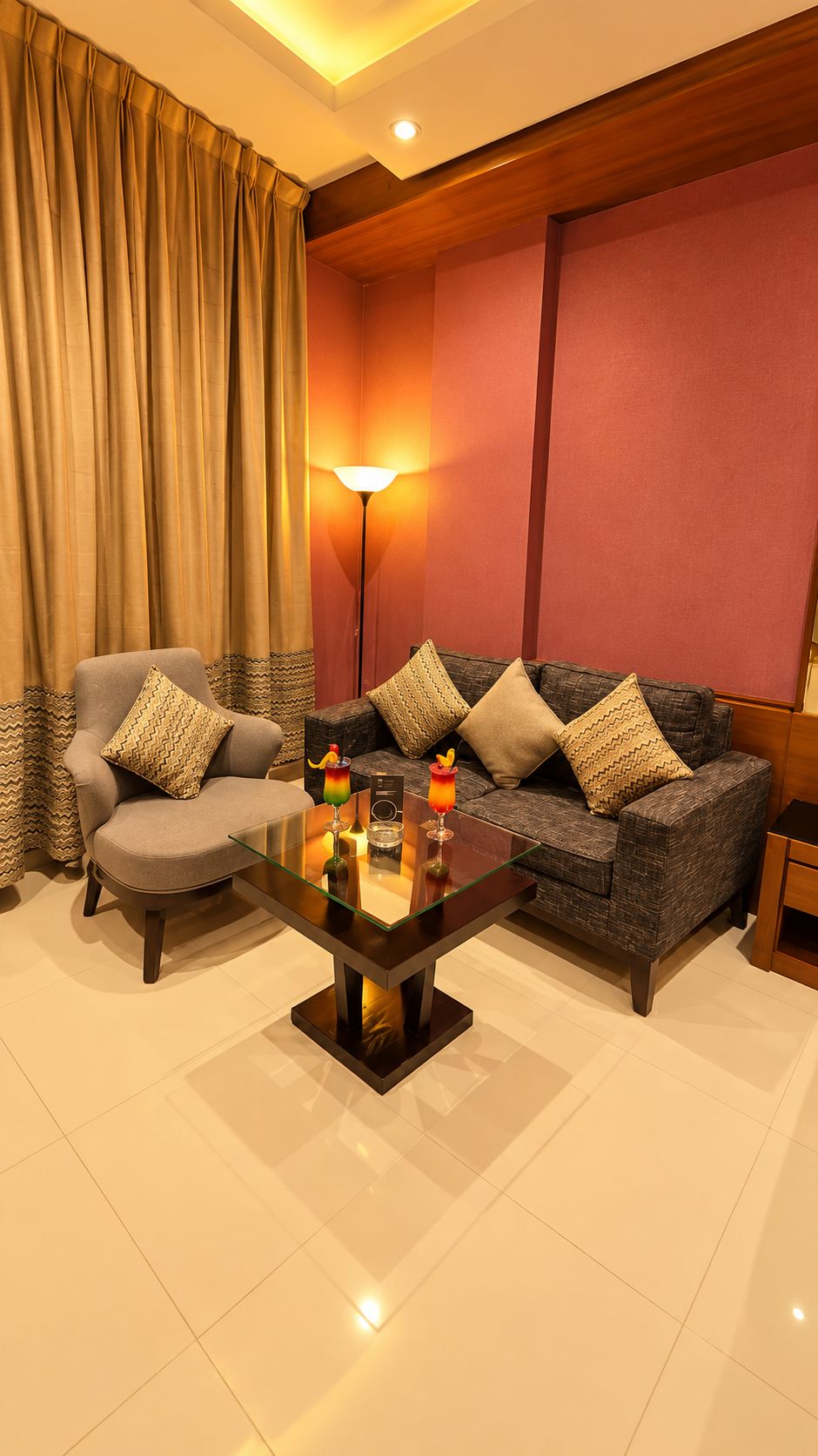 Un salón con sofá, sillón y una mesa de centro de vidrio con adornos.