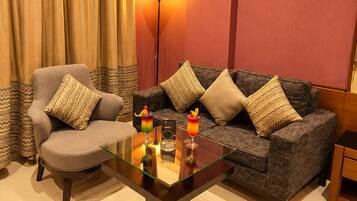 Un salón con sofá, sillón y una mesa de centro de vidrio con adornos.
