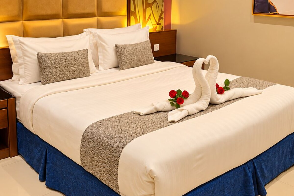 A hotel room with a large bed, a headboard with a textured panel, a wall-mounted artwork, and a decorative wall panel.