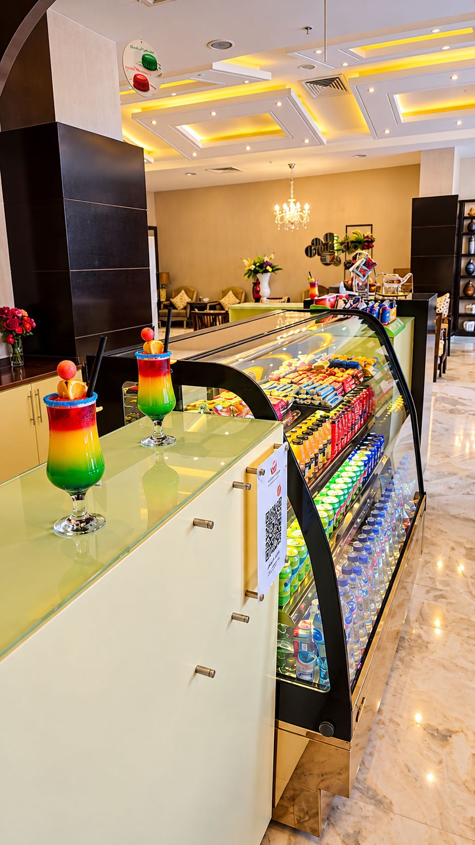 Um saguão de hotel com uma vitrine de vidro repleta de lanches e um código QR para acesso ao cardápio digital.