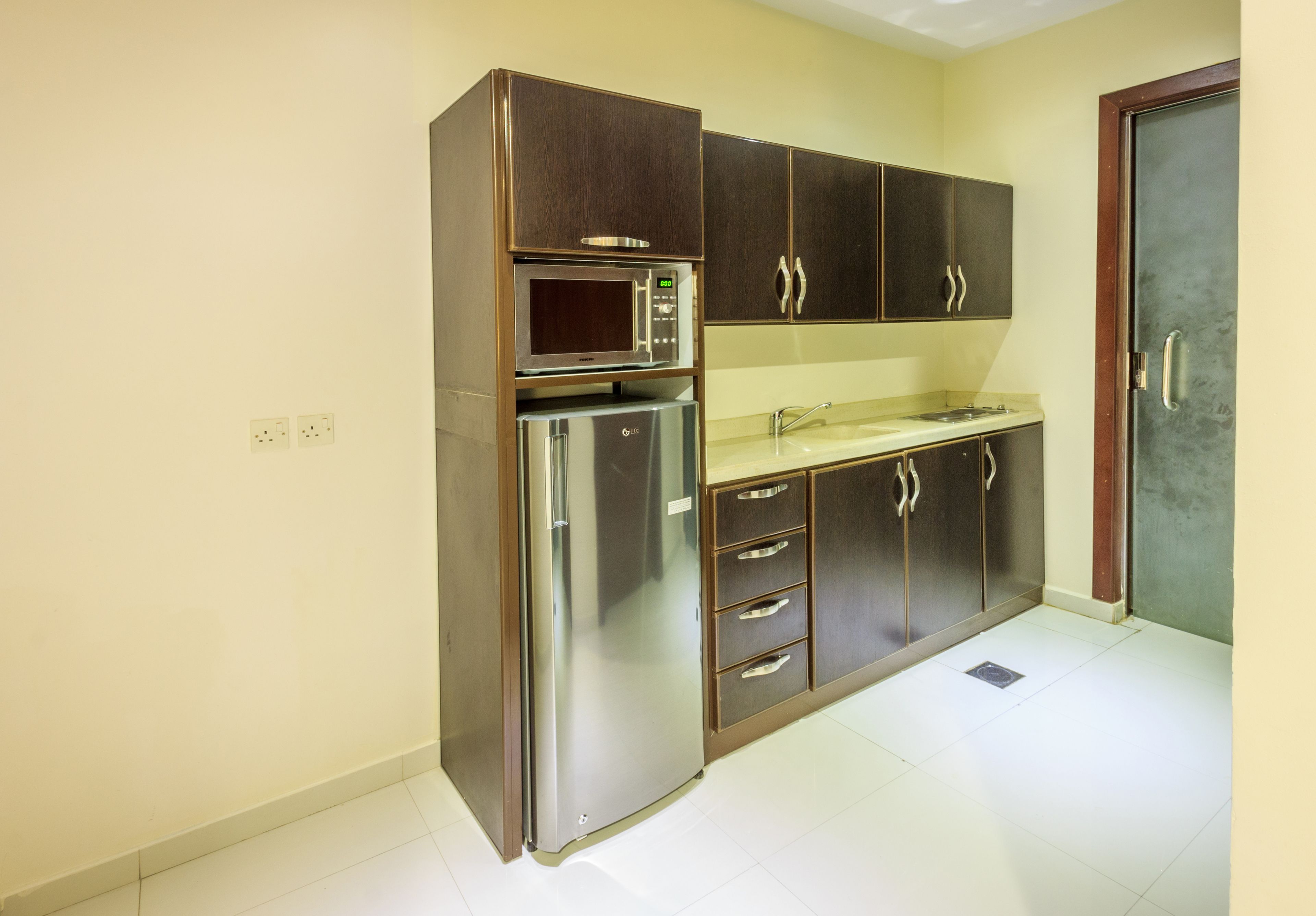 A compact kitchen with a built-in microwave, a stainless steel refrigerator, and wooden cabinets.