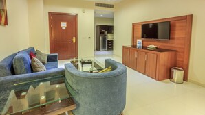A living room with a sofa, a glass coffee table, a blue armchair, a wooden cabinet, and a television mounted on the wall. - Al Muhaidb Residence Al JAWAZAT  1 - Economic (Riyadh)
