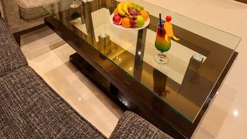 A hotel room with a glass coffee table, a sofa, a desk with a chair, a television, and a large window with curtains.