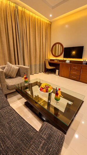 A hotel room with a glass coffee table, a sofa, a desk with a chair, a television, and a large window with curtains. - Al Muhaidb Residence Al JAWAZAT  1 - Economic (Riyadh)
