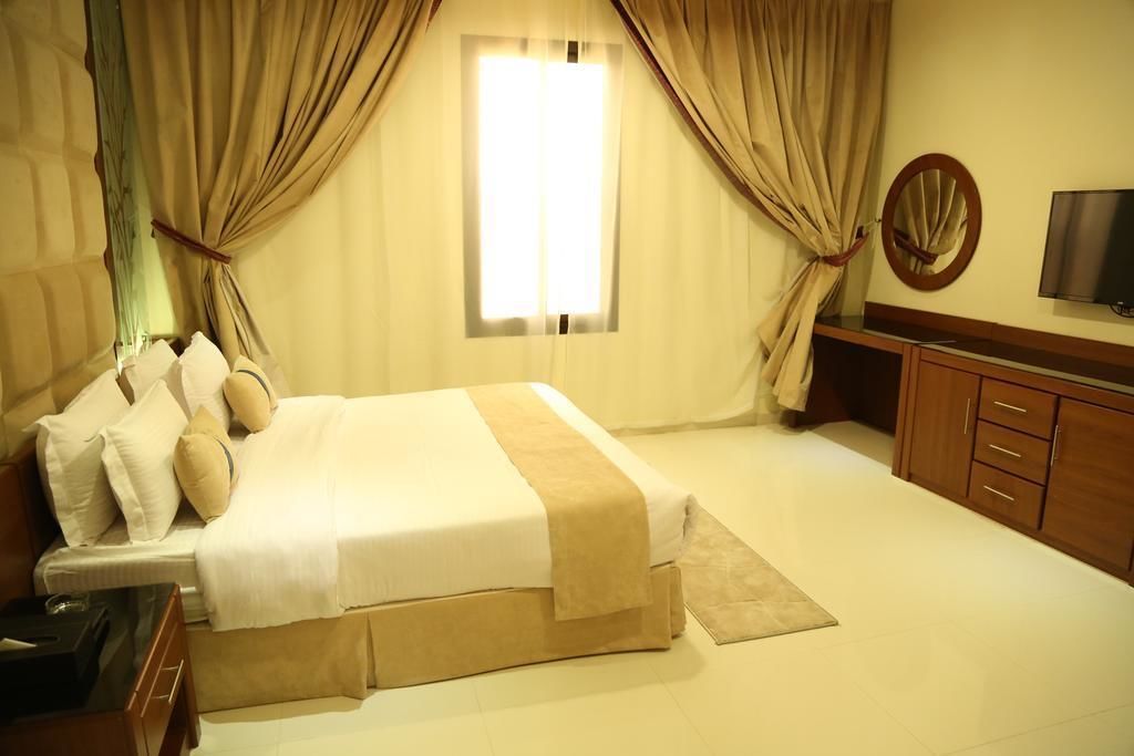 A hotel room with a large bed, a TV, a wooden cabinet, and a window with curtains.