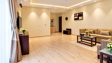 A modern living room with a wooden floor, a sofa, a coffee table, and a kitchen in the background.