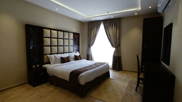 Habitación de hotel moderna con una cama grande, un televisor y un ventanal con cortinas.