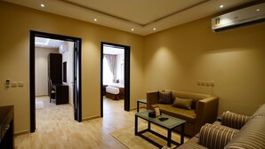 A modern living room with a sofa, a coffee table, and a TV. There is a door leading to a bedroom with a bed and a bathroom with a shower.