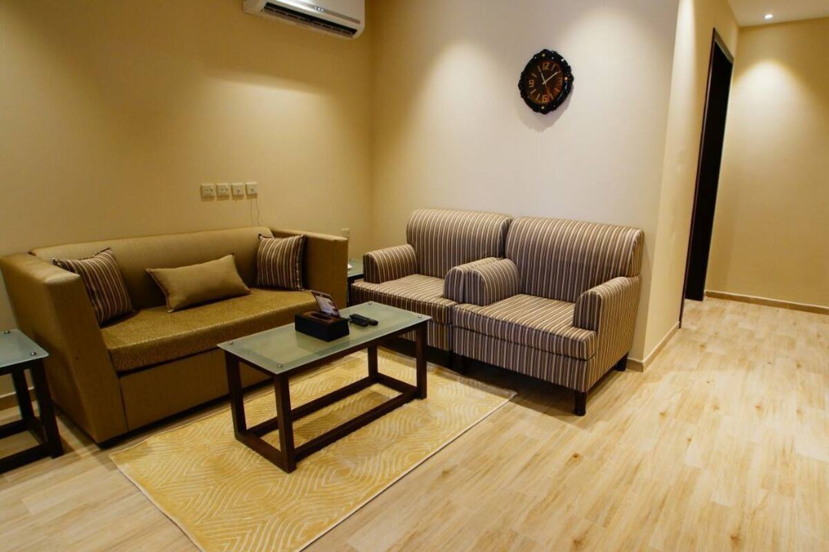 A living room with a sofa, armchair, coffee table, and a wall clock.