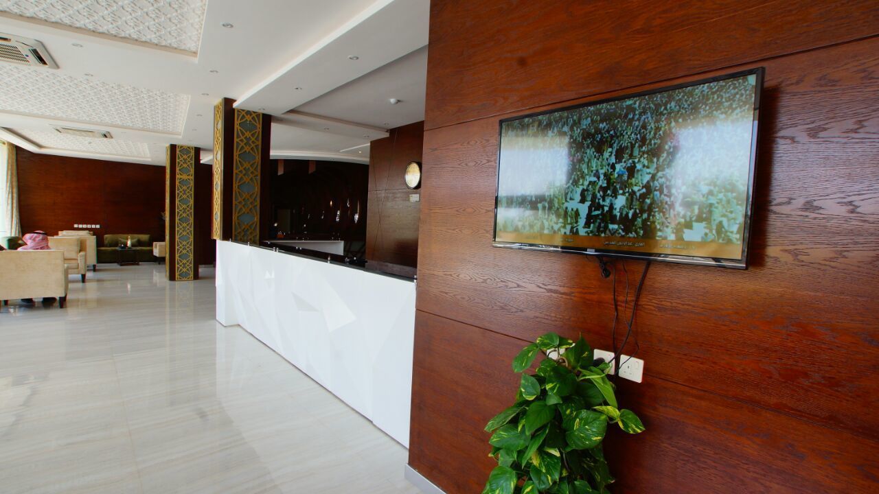 A modern lobby with a reception desk, seating area, and a large flat-screen TV mounted on a wooden wall.